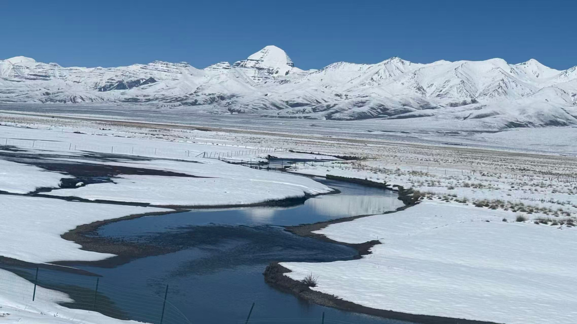 A river winding through a snow-covered plain with mountains in the distance