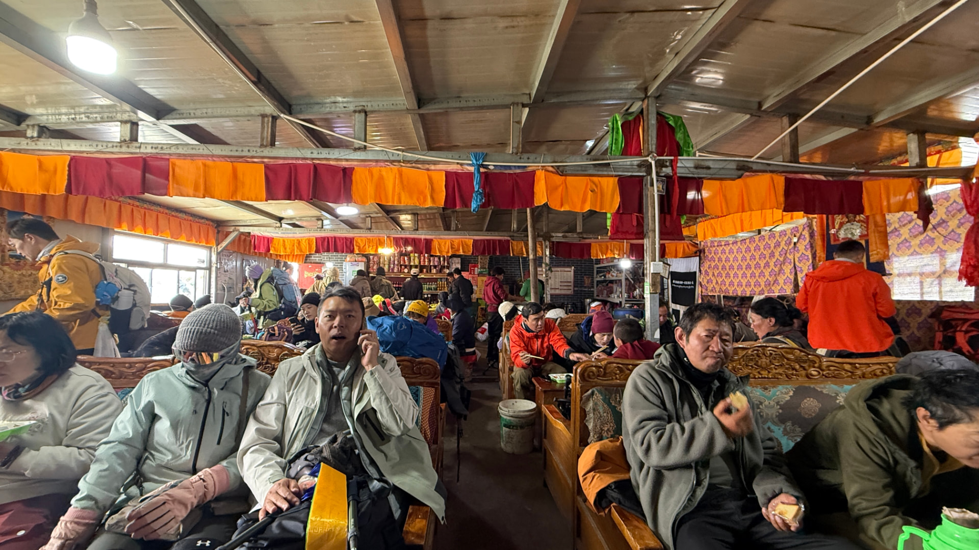 Pilgrims resting inside a busy tea house decorated with colorful prayer flags