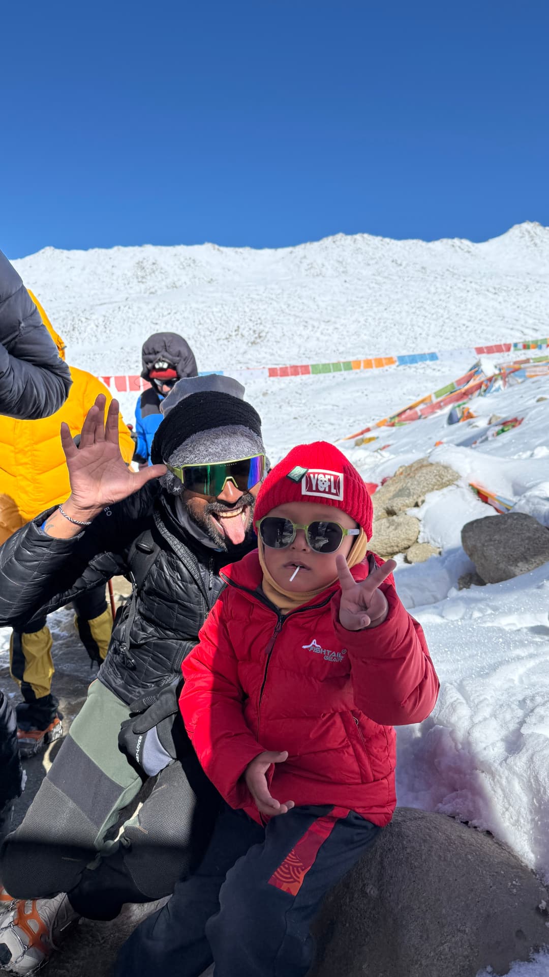 Kaivan smiling with a young pilgrim in red winter clothing amid the snow at Dolma La